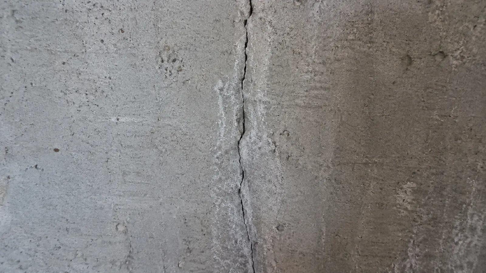A vertical crack in a poured concrete foundation wall with white mineral staining down both sides.