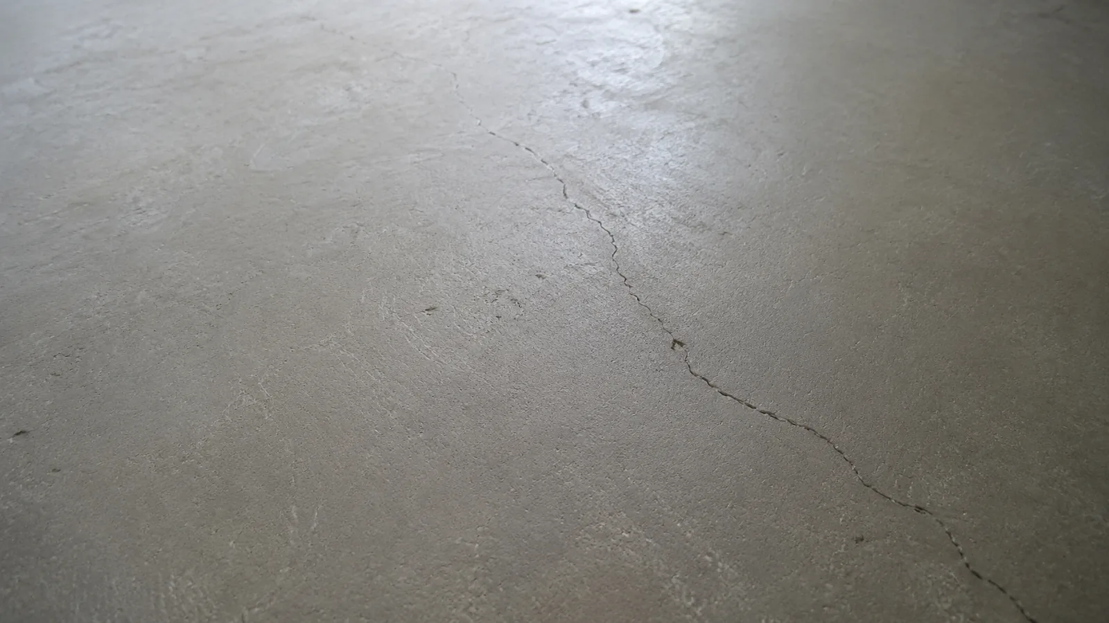 A thin crack running across a bare concrete basement floor.