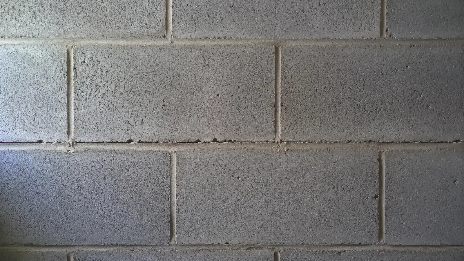 A close view of a concrete block wall with a fine horizontal crack running along the mortar joint.