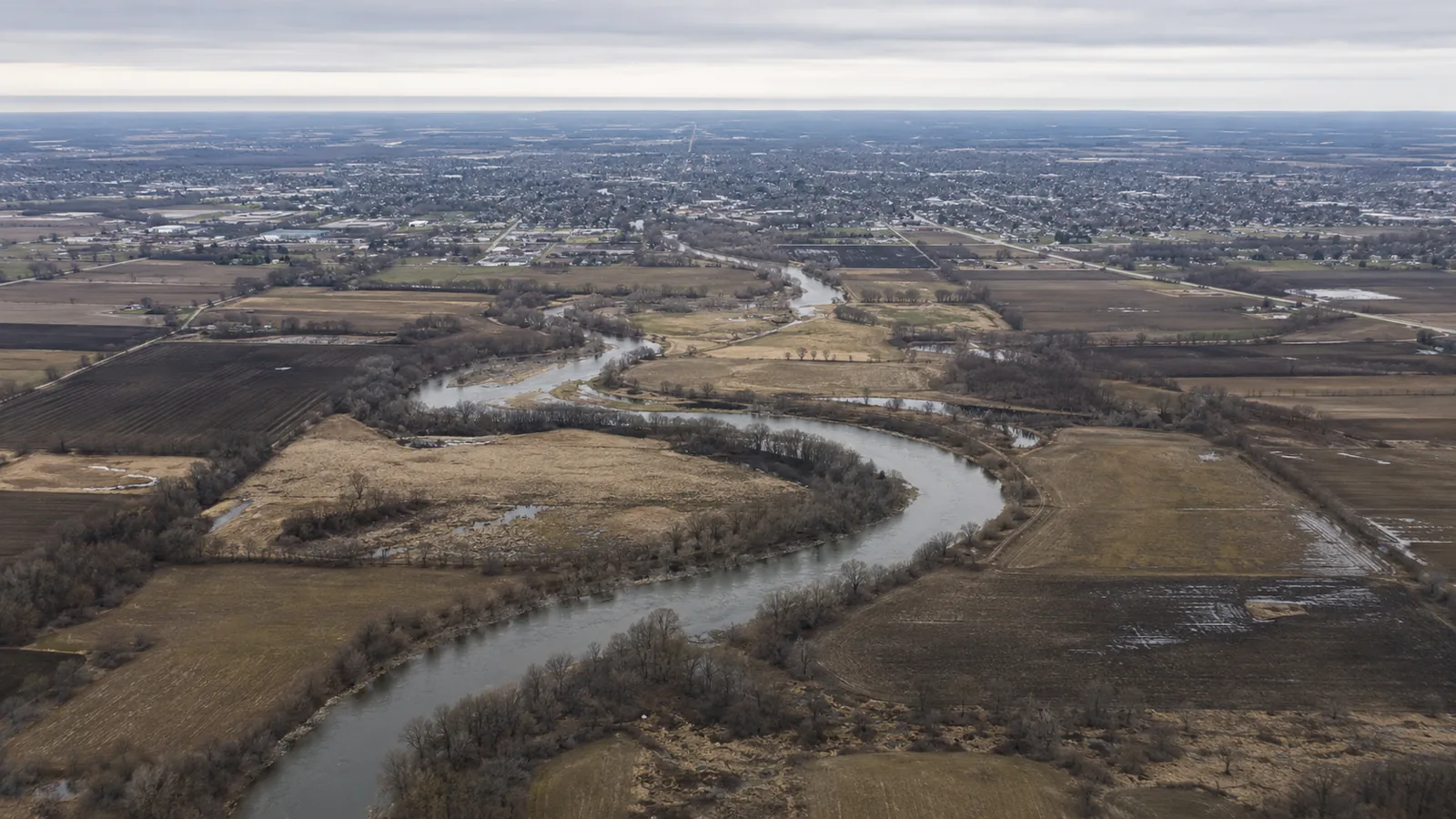 An aerial view of a river winding through farmland with a town beyond.
